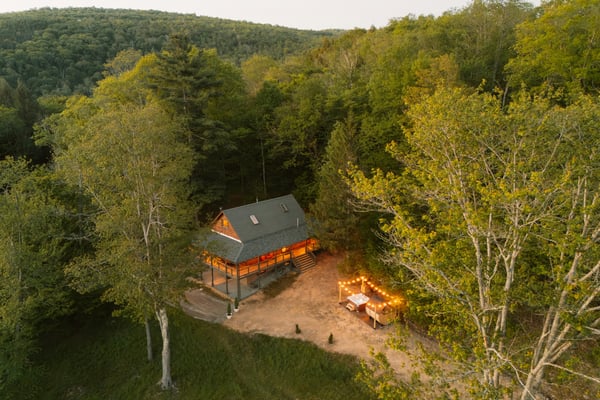 Aerial view of a cabin glowing at dusk surrounded by trees